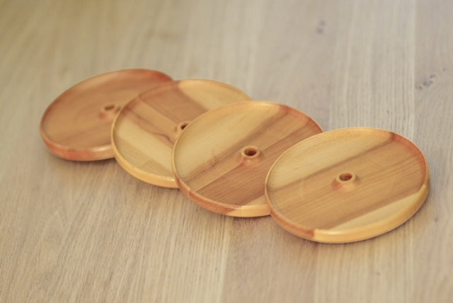 Ensemble de quatre couvercles d’apéro ronds en érable avec trou pour paille, disposés en diagonale sur une table en bois.