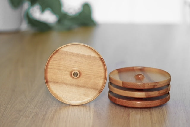Ensemble de quatre couvercles d’apéro en érable avec trou pour paille, dont trois empilés et un présenté debout sur une table en bois.