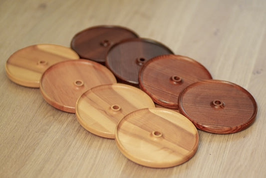 Quatre couvercles d’apéro en érable et quatre en frêne torréfié, ronds avec trou pour paille, présentés sur une table en bois.