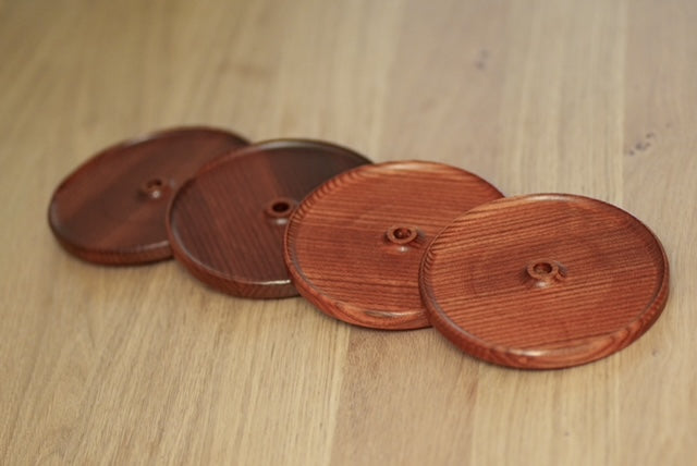 Ensemble de quatre couvercles d’apéro ronds en frêne torréfié avec trou pour paille, disposés en diagonale sur une table en bois.
