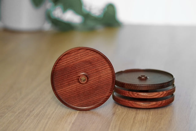 Ensemble de quatre couvercles d’apéro en frêne torréfié avec trou pour paille, dont trois empilés et un présenté debout sur une table en bois.